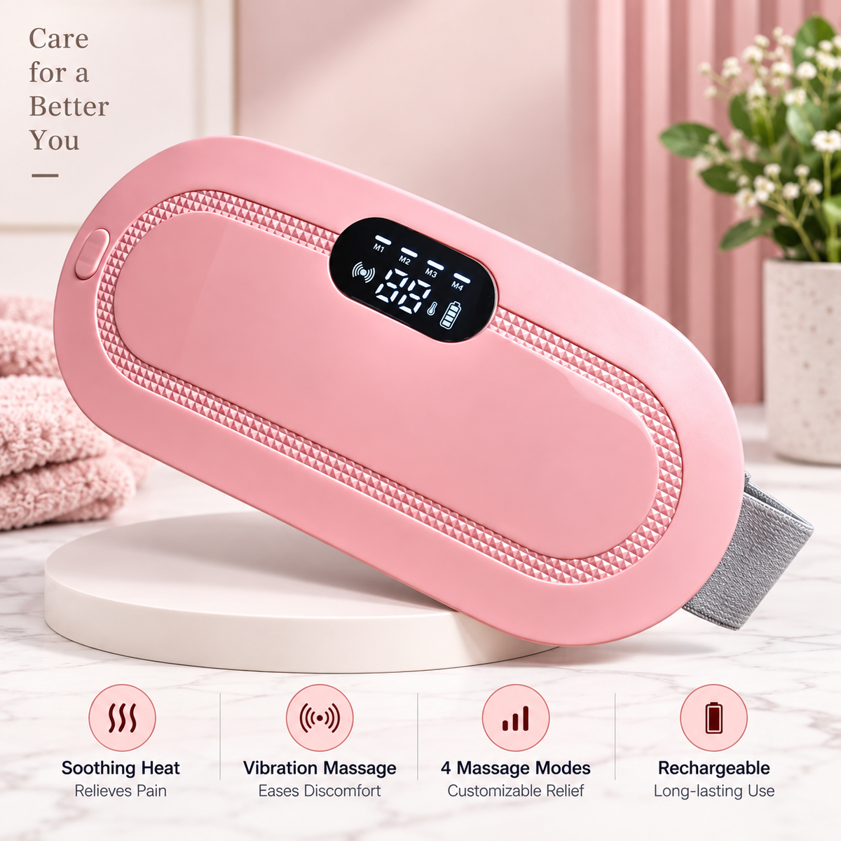 A pink handheld massage device with a digital display screen, resting on a white round tray. The background features soft pink curtains, a potted plant, and folded pink towels, with four feature icons at the bottom highlighting soothing heat, vibration massage, 4 massage modes, and rechargeable use.
